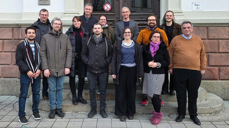 Mehrere Personen stehen auf einer Treppe vor einem Gebäude.