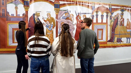 Fünf Studierende stehen vor einem großen Banner mit mittelalterlichen Wandmalereien..