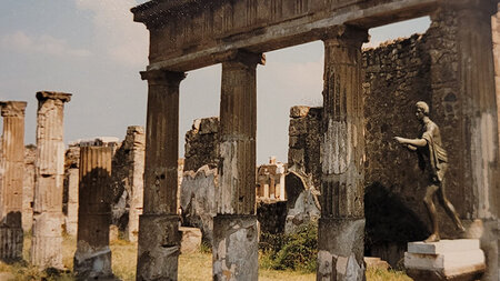 Eine Skulptur steht vor Ruinen eines Hauses mit Säulen. 