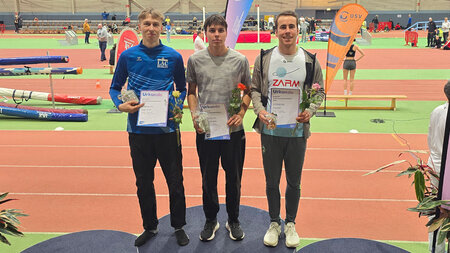 drei Männer stehen auf einem Podest mit Medaillen und Urkunden in der Hand