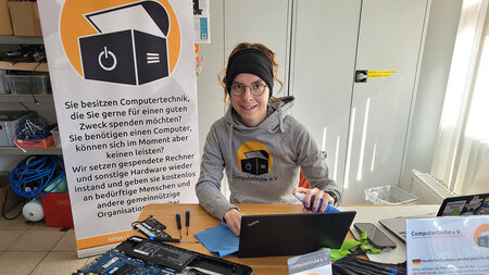 Eine Frau sitzt an einem Tisch und reinigt einen Laptop.