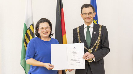 Eine Frau und ein Mann stehen nebeneinander und halten eine Urkunde in den Händen. 