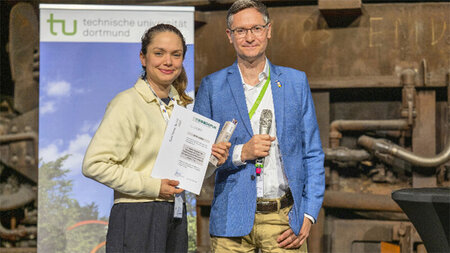 Eine Frau mit einer Urkunde in der Hand steht neben einem Mann.