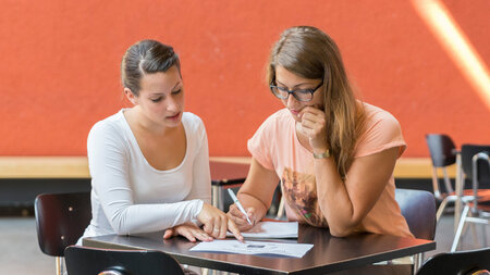 Zwei junge Frauen sitzen an einem Tisch.