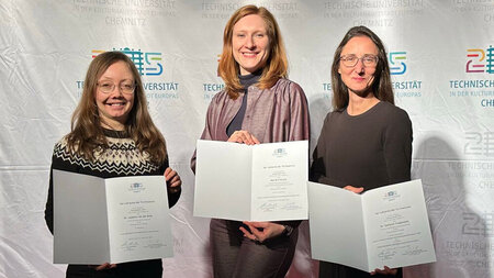Drei Frauen, die Urkunden in den Händen halten, stehen nebeneinander.