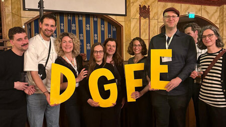 Mehrer Personen stehen in einem Foyer und halten die großen gelben Buchstaben D, G, F und E in den Händen.