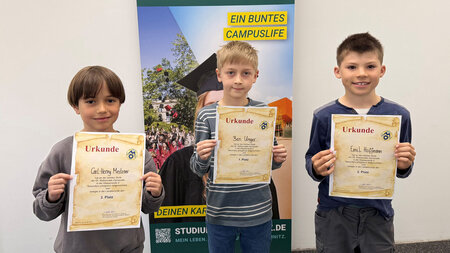 Drei Kinder stehen mit einer Urkunde in der Hand nebeneinander