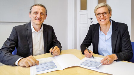 Ein Mann und eine Frau sitzen an einem Tisch und unterzeichnen Dokumente.