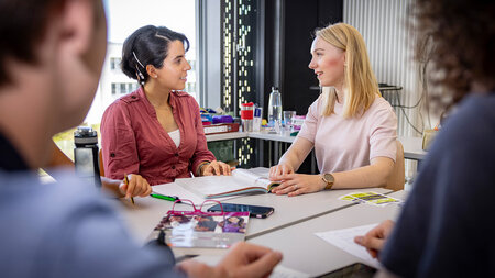 Zwei Frauen sitzen an einem Tisch und sprechen miteinander.