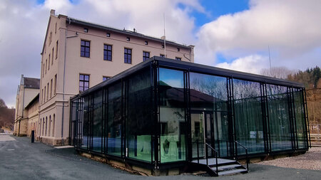 Ein Glasgebäude grenzt an ein historisches Bahngebäude.