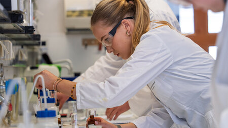 Eine Schülerin im weißen Kittel experimentiert mit einem Reagenzglas im Labor.