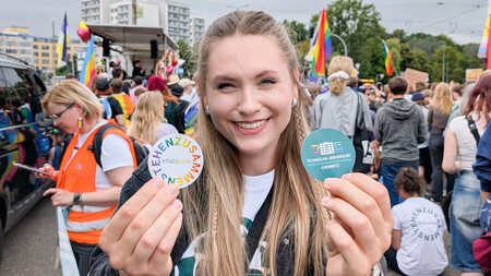 Eine blonde Frau hält zwei beschriftete Aufkleber hoch.