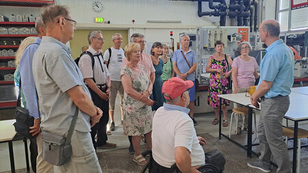 Mehrere Persionen stehen in einer Versuchsfeldhalle und h�ren einem Mann zu.