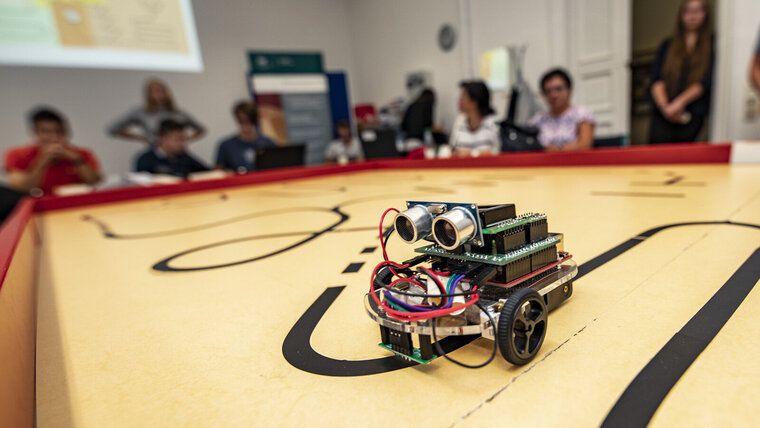 Ein kleiner Roboter rollt über einen Tisch, auf dem Markierungen zu sehen sind.