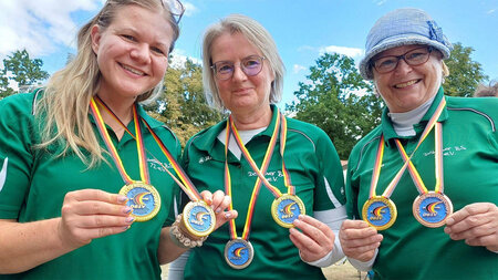 Drei Frauen halten jeweils zwei Medaillien in den Händen.