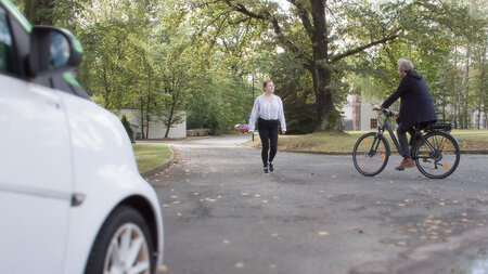 Ein Auto, eine Fußgängerin und ein Fahrradfahrer begegnen sich an einer Kreuzung. 