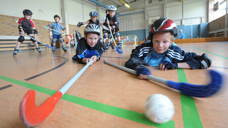 Kinder spielen Floorball in einer Sporthalle.