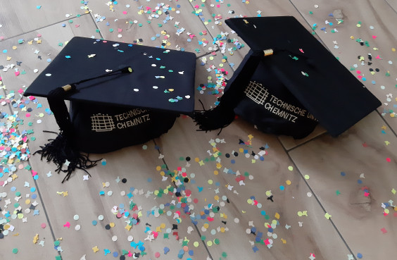 Hats with logo of Chemnitz University of Technology lying on the floor. Confetti is lying around, too.