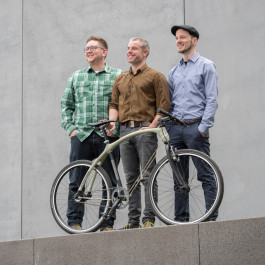 Drei Absolventen stehen nebeneinander und präsentieren ein Fahrrad.