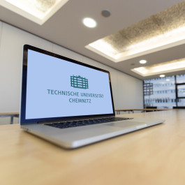 A laptop with the logo of Chemnitz University of Technology is standing on a table.