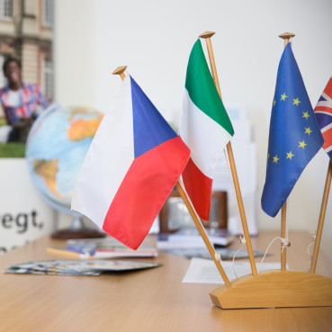 Flaggen verschiedener Länder im Vordergrund, Globus und Plakat über Erasmus-Programm im Hintergrund
