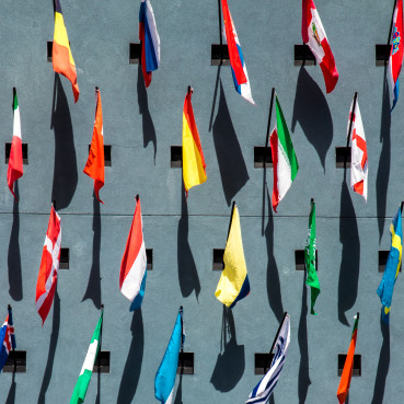 Graue Wand mit vielen unterschiedlichen Länderflaggen, die an Fahnenmasten hängen