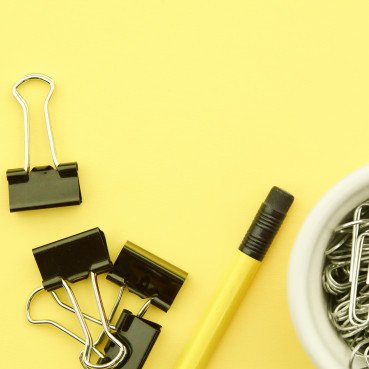 Yellow background with paper clips, a pencil and foldback clips