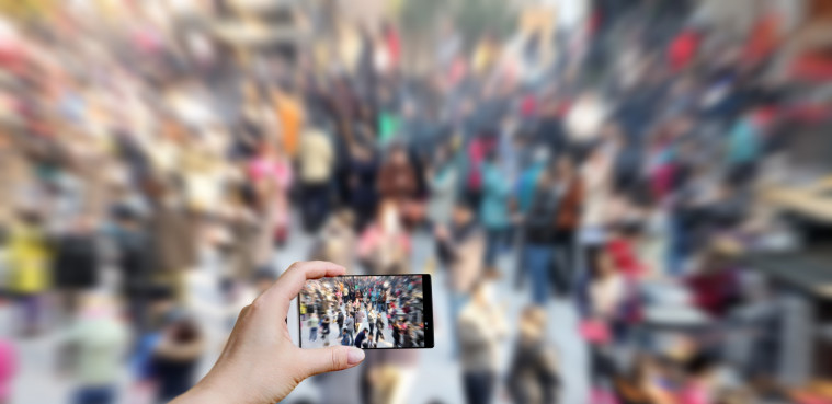 Eine Hand hält ein Handy und fotografiert eine Gruppe Personen