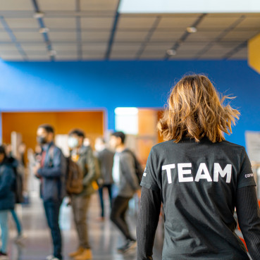 Eine Career Service Mitarbeiterin von hinten, man sieht das auf ihrem Shirt "Team" steht.