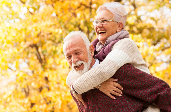 Ein fröhliches älteres Paar in einem bunten Herbstwald.