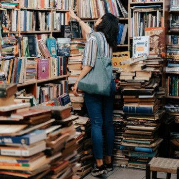 A woman standing in front of a bookshelf; there are also lots of books visible in the foreground.