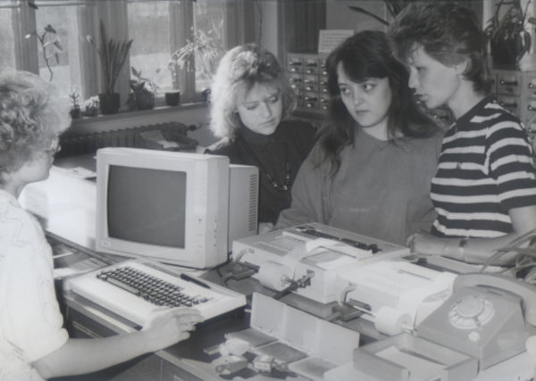 Foto: Bibliothekarin steht am ersten PC + Drucker und gegenüber stehen 3 junge Frauen, 1988 © Barbara Kretschmar