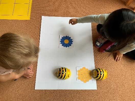 Das Bild zeigt zwei Kinder von oben, die mit dem Bee-Bot arbeiten.