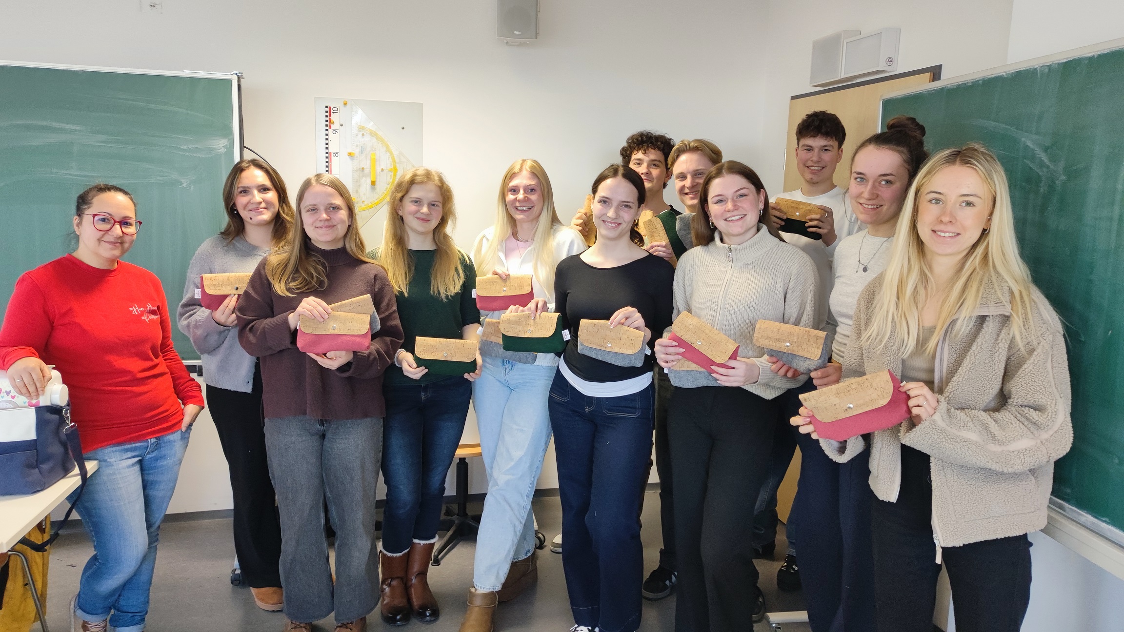 Studenten halten ihre Näherzeugnisse vor einer Tafel in Händen